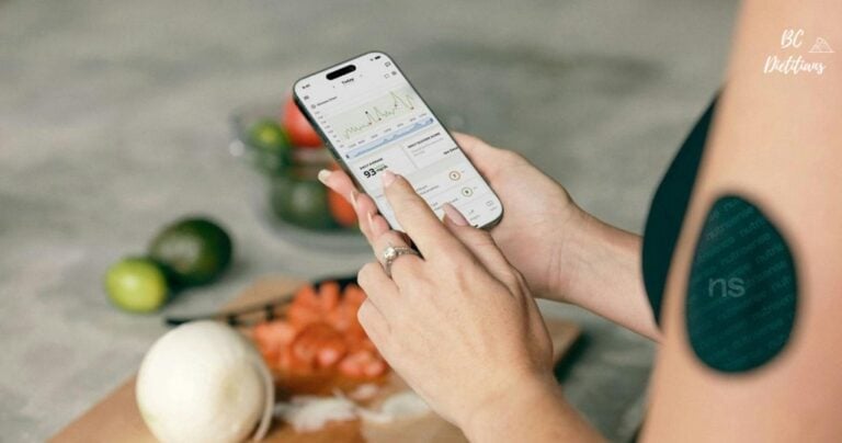 women with continuous glucose monitor on her arm looking at her blood sugar on her phone with produce laid out on a cutting board in the background